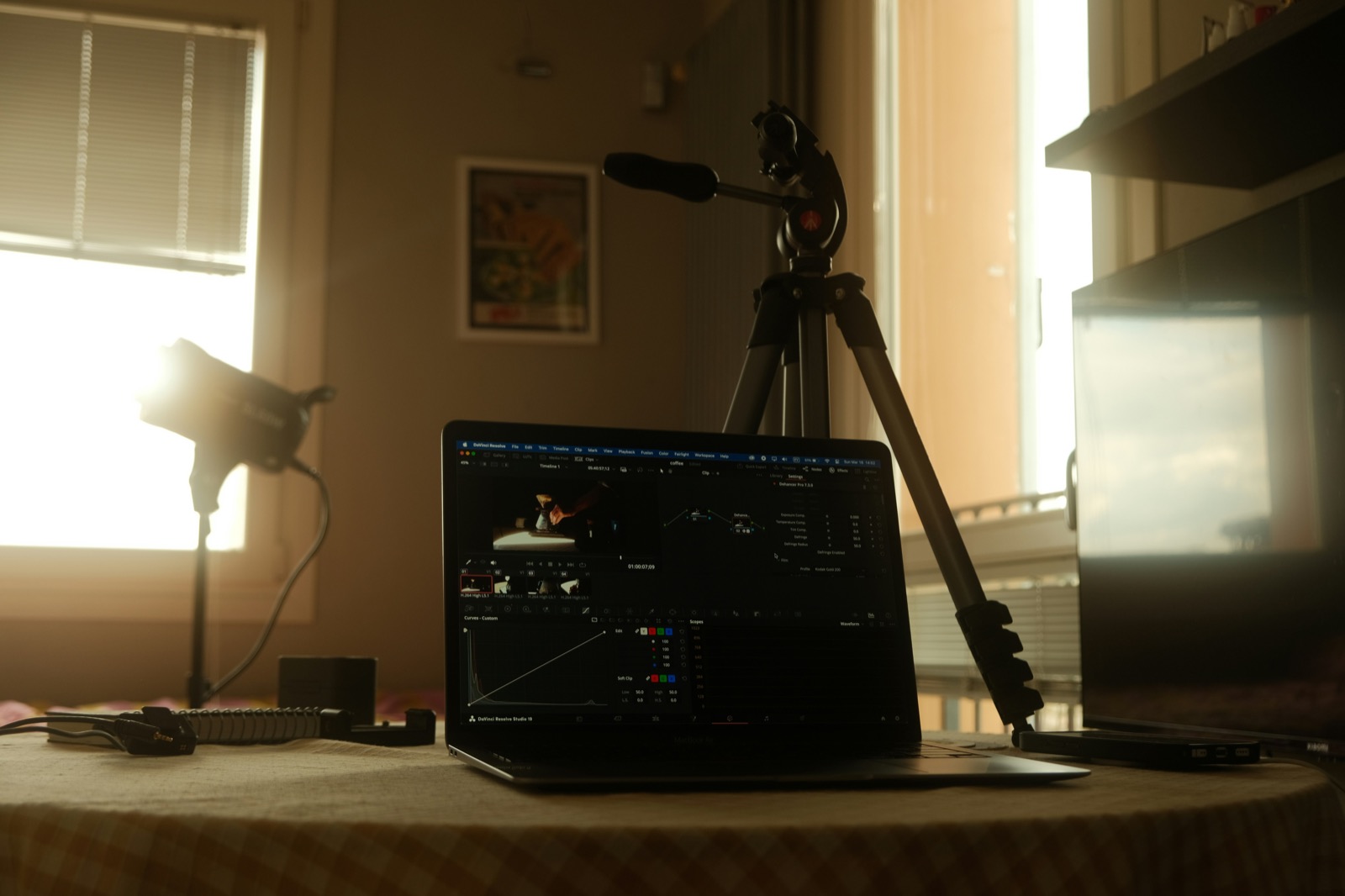 A laptop showing video colour editing beside a camera tripod